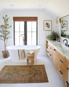 a white bath tub sitting next to a sink in a bathroom under a window with wooden cabinets