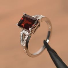 It is a natural garnet ring. The main stone is 7 mm*9 mm emerald cut.weight about 3.04 carats.The basic metal is sterling silver and plated with rhodium.To change the metal to a solid gold (white/rose) or platinum is also available, please ask for a quotation if you want.You can also go to my shop Home for more elegant rings: https://www.etsy.com/shop/godjewelry?ref=hdr_shop_menu Garnet is January birthstone More garnet rings:https://www.etsy.com/shop/godjewelry?ref=seller-platform-mcnav&sec Garnet Birthstone Ring In White Gold For Promise, White Gold Garnet Birthstone Promise Ring, White Gold Garnet Jewelry For Promise Ring, Silver Garnet Birthstone Ring For Promise, Silver Garnet Birthstone Ring With Center Stone, Silver Garnet Solitaire Ring, Silver Garnet Ring With Prong Setting, Classic Emerald Cut Birthstone Ring As Gift, Classic Emerald Cut Birthstone Ring For Gift