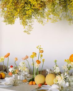 an arrangement of flowers and fruit on a table with white linens, napkins and silverware