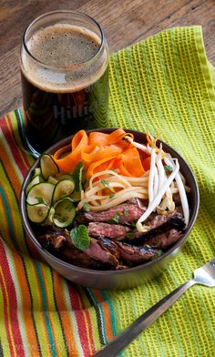 a bowl filled with meat and vegetables next to a cup of beer on top of a table