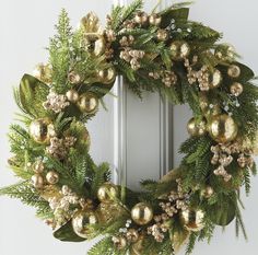 a christmas wreath with gold ornaments and greenery hanging on the front door, next to a white door