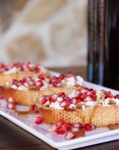 two pieces of bread topped with pomegranate on a plate next to a bottle