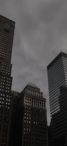 some very tall buildings in the city under a cloudy sky with dark clouds above them