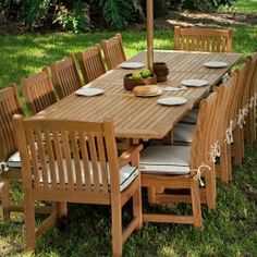 a wooden table with six chairs and plates on it in the middle of some grass