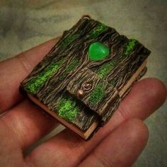 a miniature book with a green heart in the middle is held by someone's hand