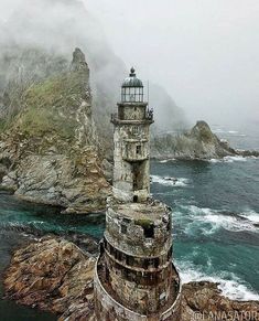 a light house sitting on top of a rocky cliff next to the ocean with fog