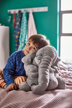 a little boy that is laying down on a bed with an elephant pillow in front of him