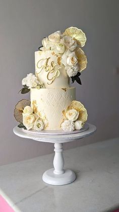 a wedding cake with white flowers and gold lettering on top is sitting on a table