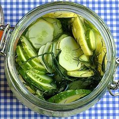 a jar filled with sliced cucumbers on top of a blue and white checkered table cloth