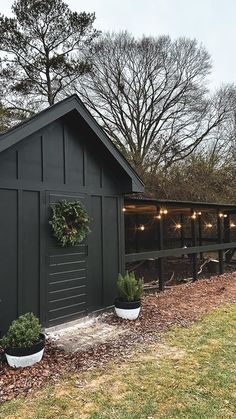 a black shed with potted plants and lights on the roof is next to a fence