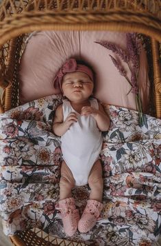 a baby is sleeping in a wicker basket with pink flowers on the pillow and blanket