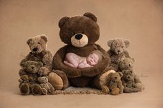 a teddy bear holding a sleeping baby surrounded by other stuffed animals on a brown background