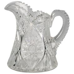 a clear glass pitcher with an intricate design on the front and sides, set against a white background