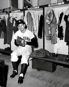 a black and white photo of a baseball player in the dugout with his glove