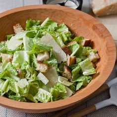 a wooden bowl filled with lettuce and croutons on top of a table