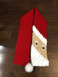 a crocheted santa claus neck tie on a wooden floor with a white pom - pom