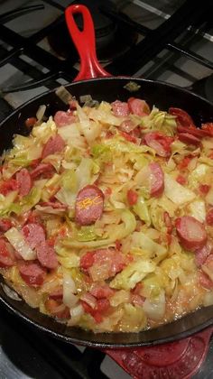 sausage and cabbage cooking in a skillet on top of the stove with a red spatula