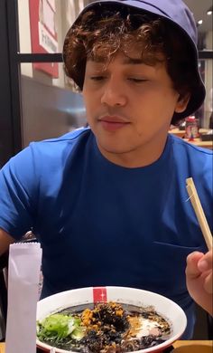 a man sitting at a table with a bowl of food and chopsticks in his hand