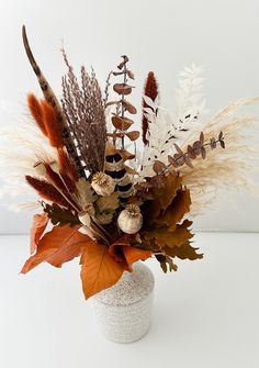 a white vase filled with lots of different types of flowers and leaves on top of a table