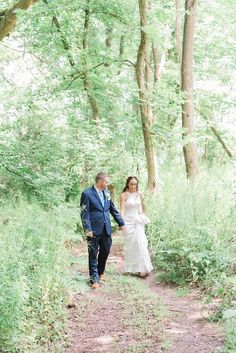 a bride and groom are walking through the woods on their wedding day, holding hands