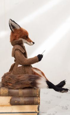 a stuffed fox sitting on top of a book with its paws in the air and it's tail curled up