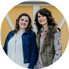 two women standing next to each other in front of a yellow wall and wooden door