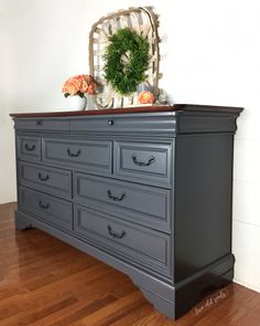 an old dresser is painted in dark gray and has a wreath on top of it