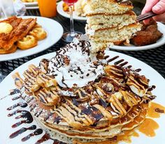 a stack of pancakes topped with whipped cream and chocolate syrup being lifted from the top