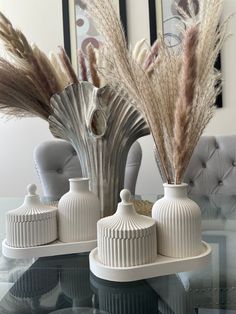 two white vases sitting on top of a glass table next to some dried grass