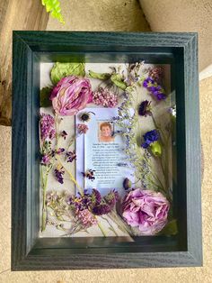 a frame with flowers and a poem in it on the floor next to a plant