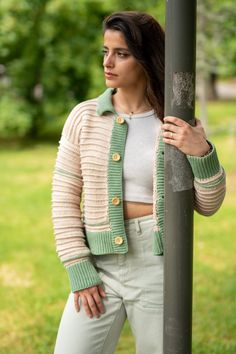 a woman leaning against a pole wearing a green and white cardigan sweater with buttons