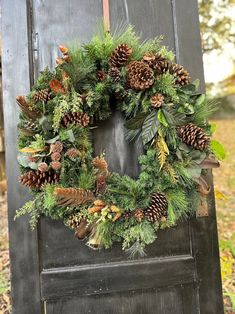 a wreath with pine cones and greenery on it is hanging from the side of an old door