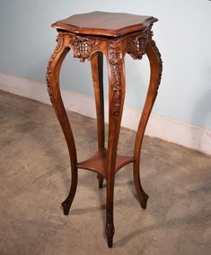 a wooden table with carvings on the top and bottom shelf, in an empty room