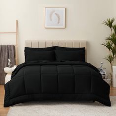 a bed with black comforter and pillows in a room next to a potted plant