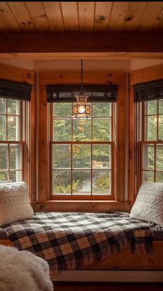 a window seat with pillows and blankets in front of it, next to two windows