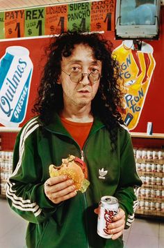 a man with long hair holding a can of soda and a sandwich in his hands