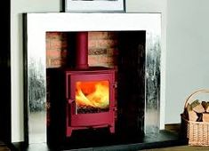 a red stove sitting inside of a fireplace next to a basket