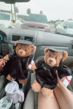 two teddy bears dressed in graduation attire sitting in the driver's seat of a car