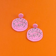 two pink and white earrings with words written on them, one says happy birthday harry