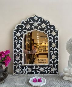 a mirror sitting on top of a table next to a vase with flowers in it