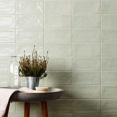 a table with a vase and brush on it next to a white tiled wall in a bathroom