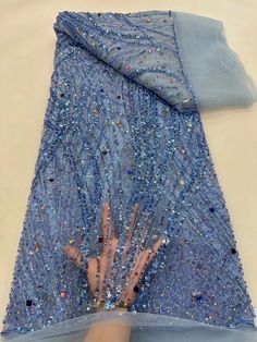 a person's hand on top of a blue dress with sequins and beads