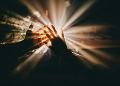 a person holding their hand up to the light coming from behind them on a dark background