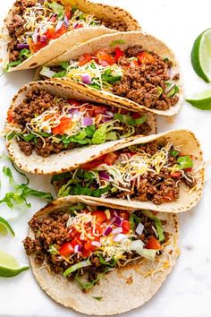 three tacos with meat, cheese and lettuce sitting on a white surface