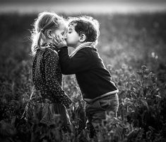 two young children kissing each other in a field