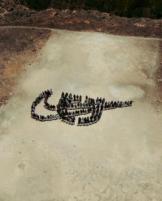 a large group of people standing in the shape of a letter on top of a dirt field