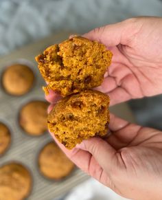 two carrot muffins being held in front of some muffin holes