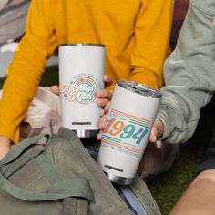 two people are holding their tumblers while sitting on the grass