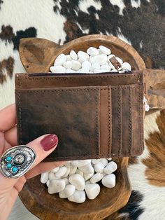 a woman's hand holding a brown wallet with white rocks in the front pocket