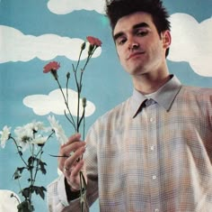 a man holding flowers in front of a blue sky with white clouds and sun behind him